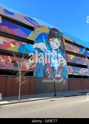 Loveland, Colorado, USA: Blick auf das Parkhaus in der Innenstadt mit Wandgemälde an der Seite. Farbenfrohes Gebäude mit mehreren Ebenen. Baum und Straßenlaterne vorne. Stockfoto