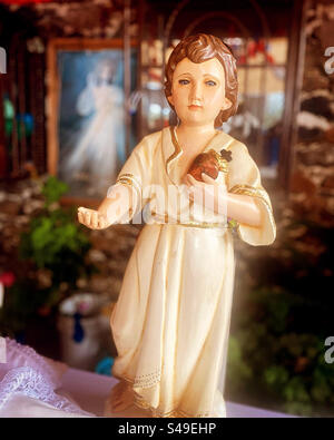 Eine Skulptur eines Jesuskindes, der das Heilige Herz vor einem Bild von Jesus de la Misericordia in der Capilla de Santiago oder der Kapelle des Heiligen Jakob in Colon, Queretaro, Mexiko hält Stockfoto