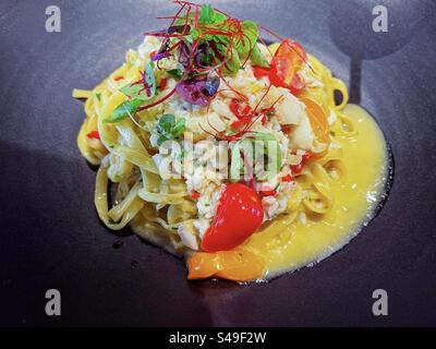 Hochwinkel-Nahaufnahme von Pasta mit Schlüsselkrabben in cremiger Sauce mit frischem Salat auf schwarzem Teller. Stockfoto