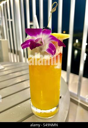 Leuchtend orangefarbenes tropisches Getränk für Erwachsene mit violetter und weißer Orchidee Stockfoto