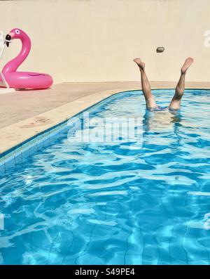 Die Beine des Mannes ragen aus dem Swimmingpool, aufblasbarer Flamingo im Hintergrund Stockfoto