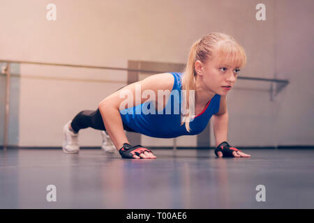 Nett Schön blond mit blauen Augen in einem blauen Sport Jersey Übungen auf dem Boden. Mädchen Athlet, Push-ups in der Turnhalle. Stockfoto