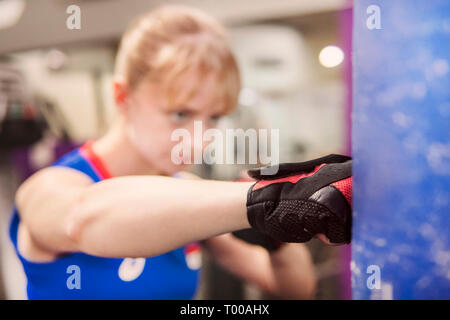 Nahaufnahme der muskulöse Frau lernen mit Fäusten, zuhause zu schlagen. Üben Hits. sparring. Der Boxsack Punch. Die blonde Sportlerin Züge h Stockfoto