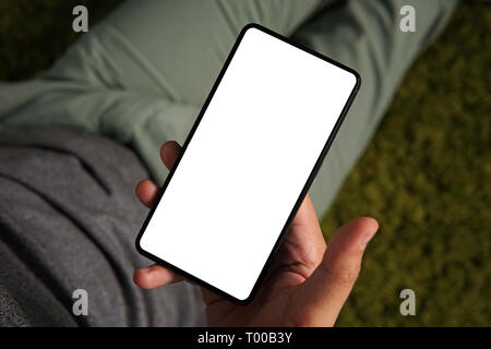 Eine Top-down-handshot eines jungen Mannes im weissen Bildschirm eines Smartphones. Mann hält das Smartphone, das in der Hand. Person ist on-line von seinem Telefon Stockfoto