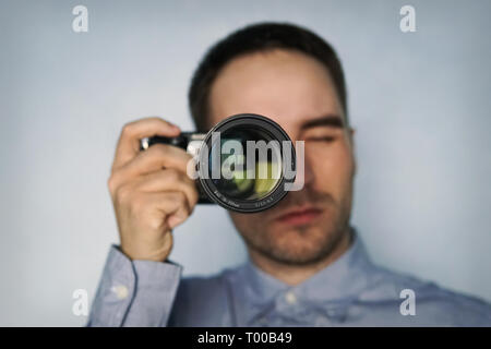 Professionellen Fotografen. Portrait von selbstbewussten jungen Mann im Hemd die Hand auf Kamera auf Stativ beim Stehen vor grauem Hintergrund Stockfoto