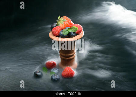 Shisha Kopf mit Beeren auf schwarzem Hintergrund in Rauch gefüllt Stockfoto