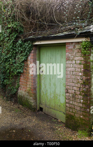 Eine verfallene hölzerne Tür, grün lackiert, auf einer alten Backstein gebaut. Stockfoto