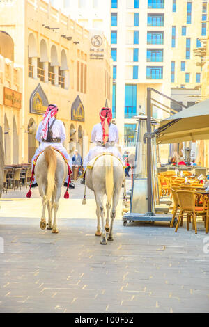 Doha, Katar - Februar 20, 2019: zwei Polizisten zu Pferde in traditioneller Kleidung im Old Souq Waqif reiten Weiße arabische Pferde auf der Fußgängerzone. Beliebte Stockfoto