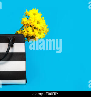 Schöne gelbe Blüten und Schwarzen und Weißen trendy female Bag auf blauem Hintergrund. Stockfoto