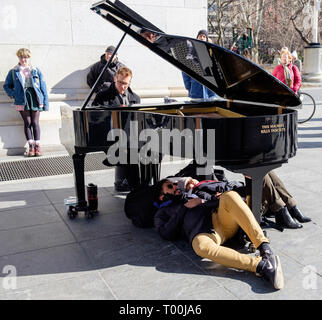 Colin Huggins spielt Klavier mit "Diese Maschine tötet Faschisten" & 2 Personen unter am Washington Square Park, Greenwich Village, Mar 2018 zur Festlegung Stockfoto