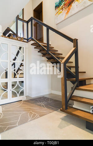 Hickoryholz Treppe mit schwarzem Metall und Holz Oberseite Klarglasgeländer führt vom Untergeschoss zum Hauptgeschoss im luxuriösen zeitgenössischen Haus. Stockfoto