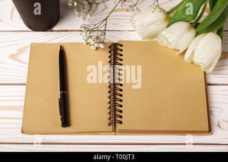 Weiße Tulpen mit einem leeren offenen Notizbuch aus Papier auf einem weißen Holz- Hintergrund. Mockup Vorlage für die Grußkarte. Flach, Ansicht von oben. Frau wor Stockfoto
