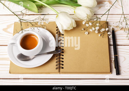 Frau Schreibtisch mit Kaffeetasse, Notizbuch aus Papier und Weiße Tulpen. Mockup Vorlage für die Grußkarte. Flach, Ansicht von oben, aus der Nähe. Blumen für Motten Stockfoto