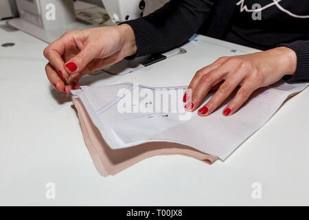 Weibliche Hände Schneider mit einem Tuch, das Muster und die Nadel in der Werkstatt Stockfoto