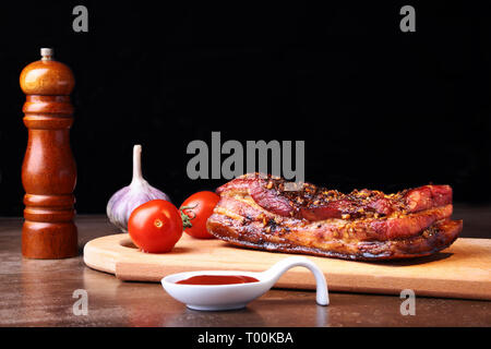 In Scheiben geschnitten gegrillte Schweinerippchen Grill Roastbeef Steak mit chimichurri Sauce und Tomaten auf Schneidebrett auf dunklem Hintergrund. Stockfoto