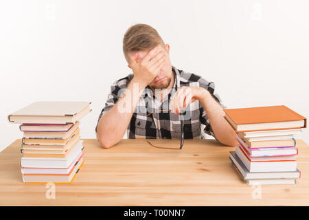 Schüler, die Untersuchung und die Bildung Konzept - Müde junge Mann am Tisch sitzen mit Bergen von Büchern Stockfoto