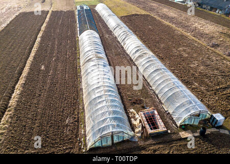 Luftaufnahme von langen gewölbten Gewächshäuser mit Polyethylen in gepflügt Frühling Feld abgedeckt. Agrar- und Landwirtschaft. Stockfoto