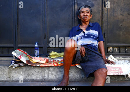 ANTIPOLO CITY, Philippinen - 9. MÄRZ 2019: Eine ausgereifte Filipino Mann ruht auf einem Bürgersteig und posiert für die Kamera. Stockfoto