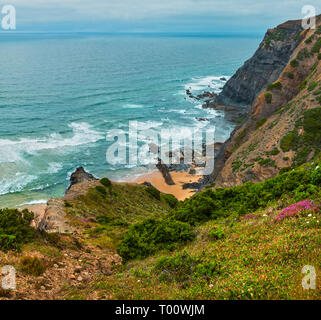 Sandstrand mit felsigen Bergrücken trübes Wetter Aussicht auf Sommer Atlantic an der felsigen Küste (Costa Vicentina, Algarve, Portugal). Und Ocean Surf Wellen. Stockfoto