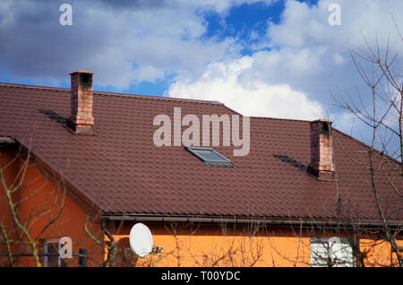 Dachfenster und Ziegel Rohre auf dem Dach. braun Metall Schindeln, blauer Himmel. Stockfoto