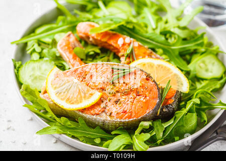 Gebratene rote Fische mit Rucola und Gurkensalat in eine weiße Platte. Stockfoto