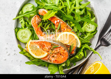 Gebratene rote Fische mit Rucola und Gurkensalat in eine weiße Platte, Ansicht von oben. Stockfoto