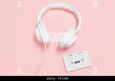 White Kassette und Kopfhörer auf einem rosa Hintergrund. Party 90 s Konzept. Stockfoto