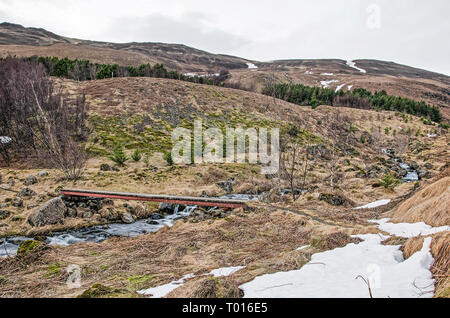 Isländische Landschaft im späten Winter mit einer schmalen Holzbrücke über einen kleinen Bach mit kleinen Wasserfällen und Stromschnellen Stockfoto