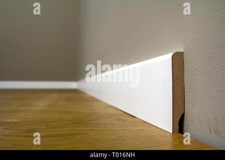Holz- oder Kunststoff Weiß, Sockel Installation in großen leeren Raum auf Holzboden und weiß verputzt verputzten Wänden Hintergrund. Details im Innenraum. Stockfoto