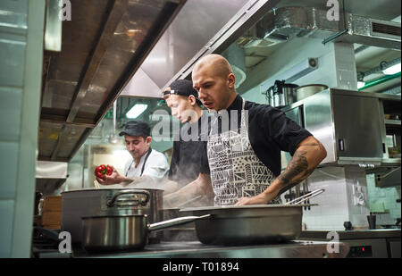 Bei der Arbeit konzentriert. Professionelles team von Chef und zwei junge Assistenten Kochen in einem Restaurant Küche. Essen Vorbereitung Konzept Stockfoto