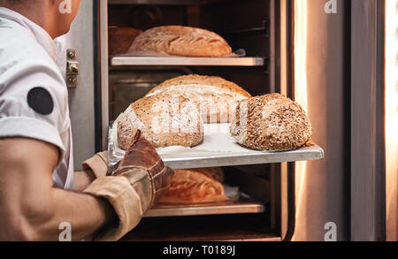 Lecker und frisch. Baker's Hände in Arbeitshandschuhen, frisch gebackenes Brot aus dem Ofen in der Küche. Bäckerei Konzept. Stockfoto