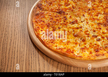 Pizza mit Käse heiß serviert und lecker auf Holzplatte auf Tisch. Schnelle und kostengünstige Mahlzeit Stockfoto