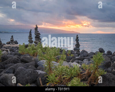 Blick von der steinigen Küste über Stein Haufen auf den Sonnenuntergang über dem Meer auf der Insel Sao Miguel, Azoren, Portugal Stockfoto