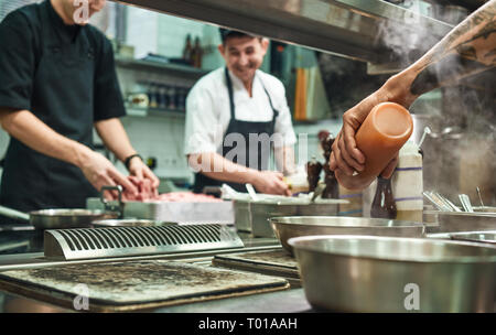 Professionelles team. Fröhlicher junger kocht das Essen gemeinsam in einem Restaurant in der Küche. Kochen Konzept Stockfoto