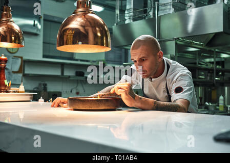 Feine Arbeiten. Zuversichtlich Küchenchef dekorieren leckere Schokolade Kuchen, während in einem Restaurant in der Küche stehen. Süßwaren Stockfoto
