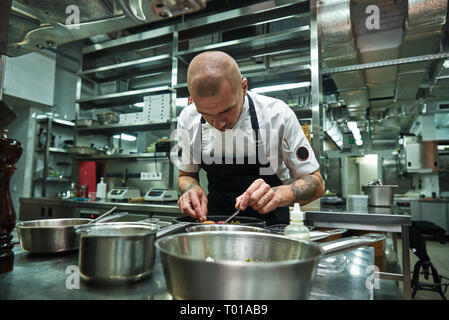 Feine Arbeiten. Junge männliche Chef mit mehreren Tattoos auf seinem Arme ist Garnieren italienische Pasta Carbonara in einem Restaurant Küche. Essen Konzept Stockfoto