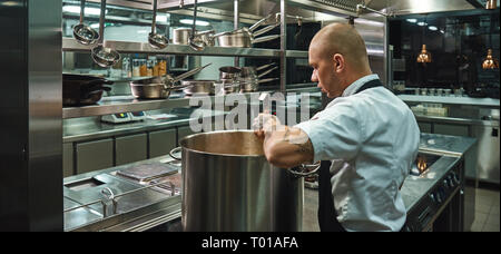 Auf seine Arbeit konzentriert. Seitenansicht des berühmten jungen Koch mit Tattoos auf seinem Arme kochen eine Suppe in einem Restaurant Küche. Kochen Stockfoto