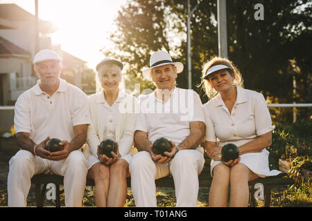 Freundliche ältere Männer und Frauen sitzen zusammen in einem Park mit Boule in der Hand. Senior Freunden zusammen sitzen auf einer Bank in einem Park. Stockfoto