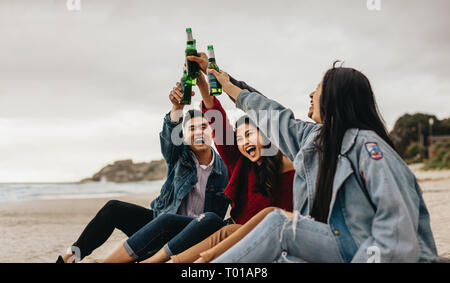 Gruppe von vier asiatischen Freunden Bier trinken am Ufer des Meeres. Junge Menschen am Strand eine Party mit Getränken. Stockfoto