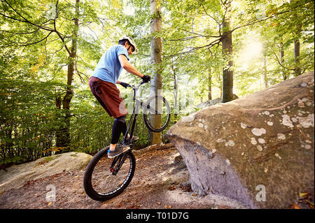 Junge portsman Radfahrer reiten auf der Rückseite Rad Trial Bike, mann Reiter balancing am Rande des Big Boulder im Wald im Sommer sonnigen Tag. Konzept o Stockfoto