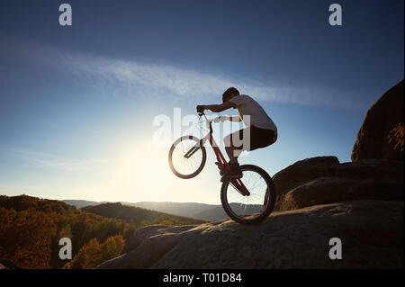 Sportsman Radfahrer stehen auf der Rückseite Rad Trial Fahrrad, mann Biker auf dem Gipfel des Berges im Sommer sonnigen Morgen. Blauer Himmel und sunris Stockfoto