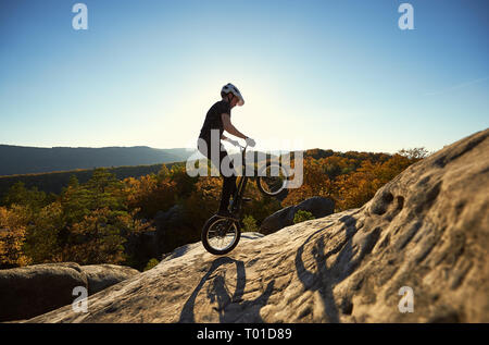 Profisportler Radfahrer springen auf Trial Fahrrad auf Big Boulder. Männliche biker die akrobatischen Stunts auf Sommerabend, blauer Himmel und sunse Stockfoto