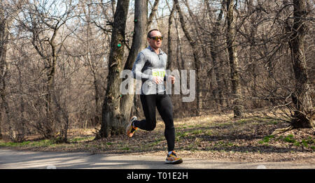 ALMATY, Kasachstan - 16. MÄRZ 2019: Ein unbekannter Mann läuft durch ein Wäldchen im Frühjahr Marathon in der Stadt Almaty, in einem Hain nach Namen Stockfoto