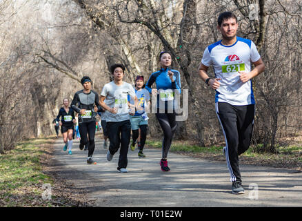 ALMATY, Kasachstan - 16. MÄRZ 2019: eine dichte Gruppe von unbekannten Männern und Frauen läuft durch ein Wäldchen im Frühjahr Marathon in der Stadt Almaty Stockfoto