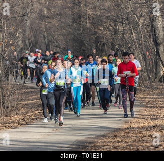 ALMATY, Kasachstan - 16. MÄRZ 2019: eine dichte Gruppe von unbekannten Männern und Frauen läuft durch ein Wäldchen im Frühjahr Marathon in der Stadt Almaty Stockfoto