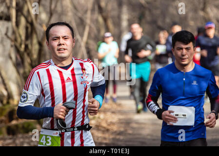 ALMATY, Kasachstan - 16. MÄRZ 2019: eine dichte Gruppe von unbekannten Männern und Frauen läuft durch ein Wäldchen im Frühjahr Marathon in der Stadt Almaty Stockfoto