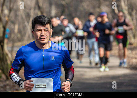 ALMATY, Kasachstan - 16. MÄRZ 2019: eine dichte Gruppe von unbekannten Männern und Frauen läuft durch ein Wäldchen im Frühjahr Marathon in der Stadt Almaty Stockfoto