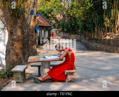 Junger buddhistischer Mönch in orange Gewand studieren an Tisch im Freien, Wat Phoy Khuay Kloster, Luang Prabang, Laos Stockfoto