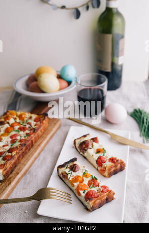 Hausgemachte Kuchen (quiche), mit Ricotta und frischen farbigen Tomaten, in Scheiben schneiden, in eine Schüssel mit goldenen Gabel schneiden, ein Glas Wein, rechteckigen Formen, frontal Stockfoto