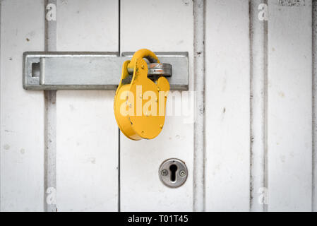 Single heavy duty Tough gelben Vorhängeschloss auf ein weißes Metall Tür mit Copyspace Bereich für Sicherheit themed Designs und Ideen gesperrt Stockfoto